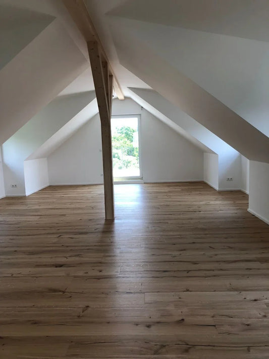Parquet à lames larges déjà poncé dans les combles, avec des pentes de toit et des poutres apparentes